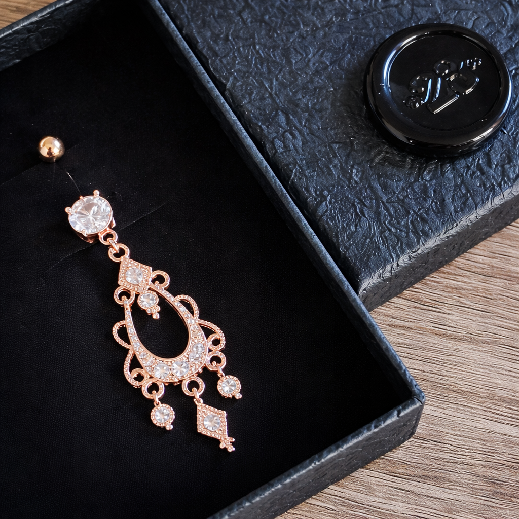 Rose gold chandelier belly ring in a black jewelry box on a wooden surface
