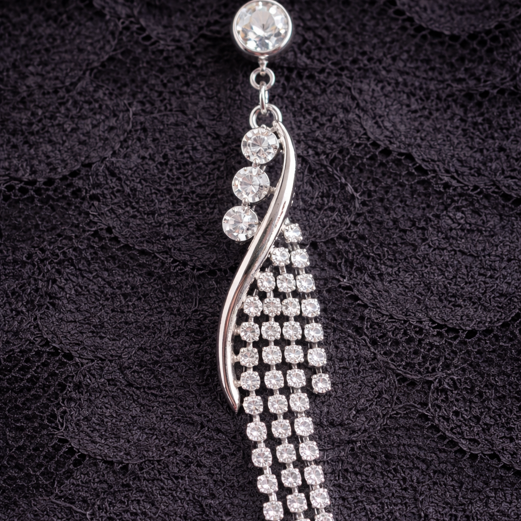 Silver navel bar with clear stones on a black textured background