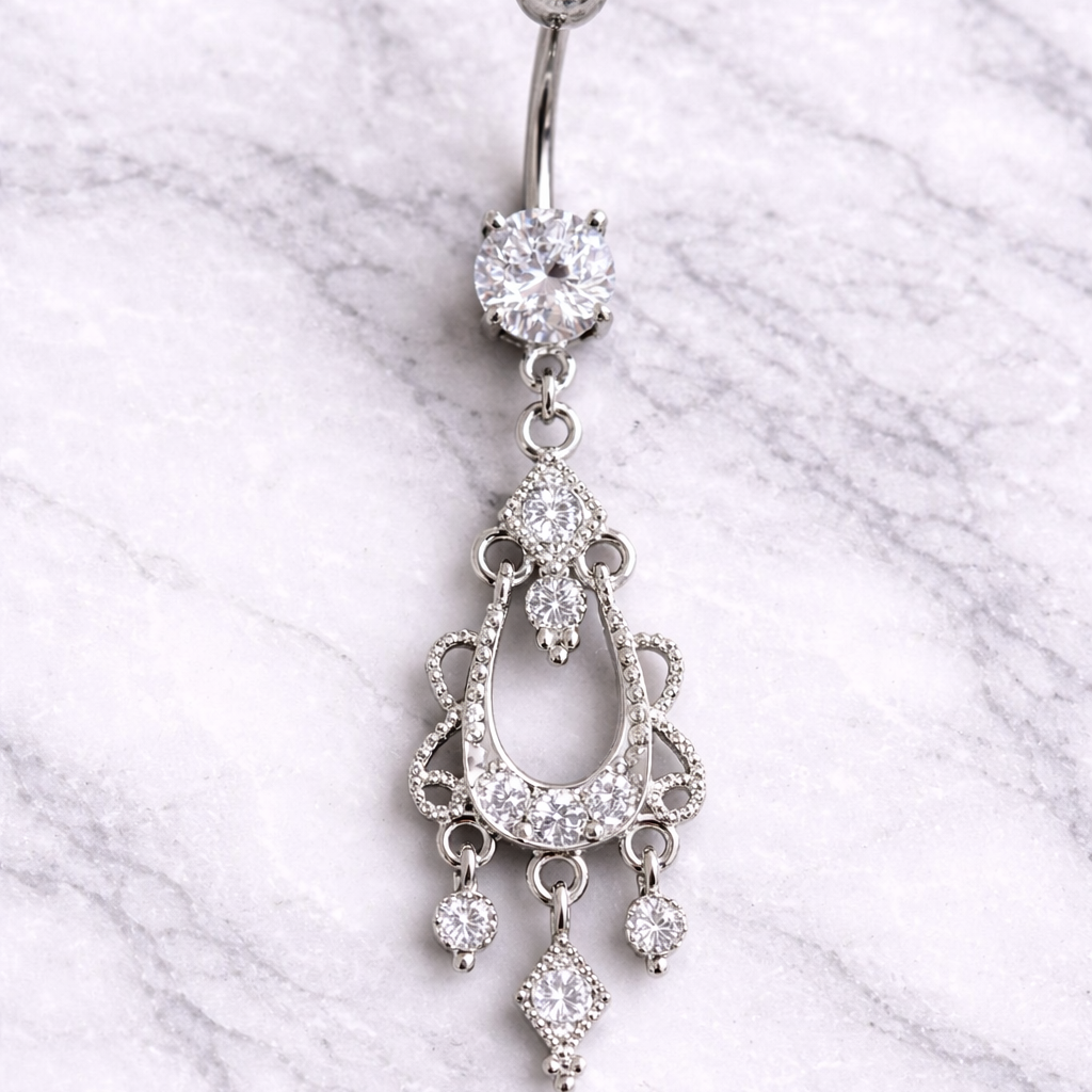 Silver belly button ring with chandelier design on a marble background