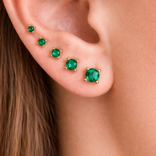 Close-up of an ear wearing gold emerald stud earrings.