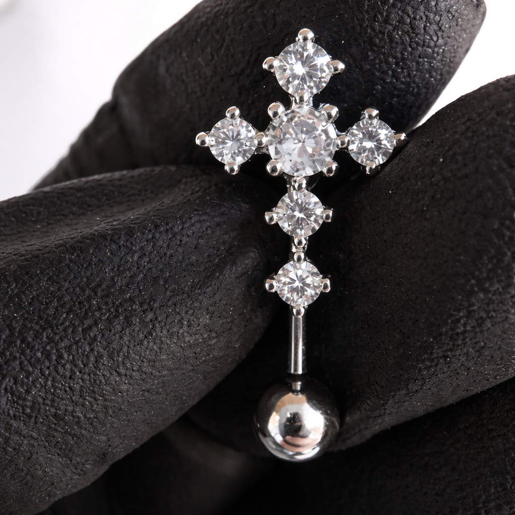 Silver cross-shaped earring with clear gemstones held by a gloved hand.