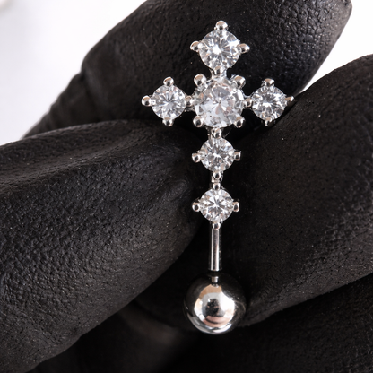 Silver cross-shaped earring with clear gemstones held by a gloved hand.