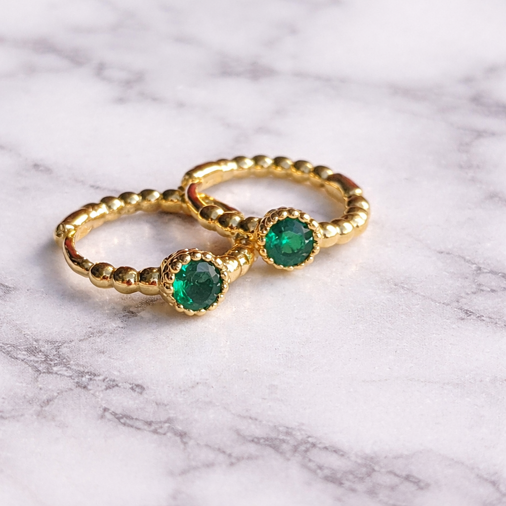 Gold rings with emerald stones on a marble surface