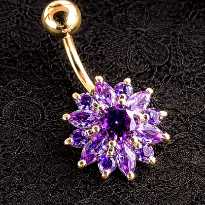 Gold belly button ring with a purple gemstone flower design on a black textured background