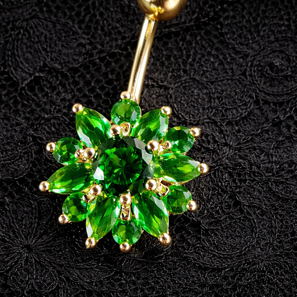 Gold belly button ring with green gemstones on a black textured background