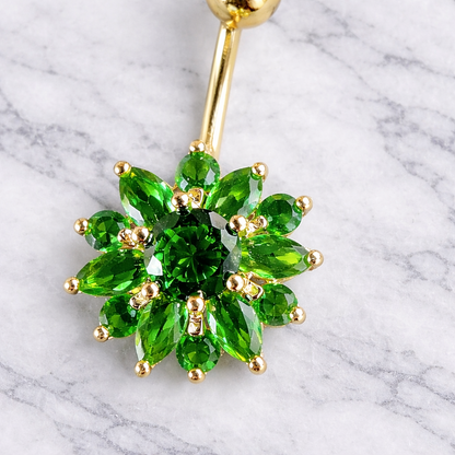 Gold belly button ring with green gemstones on a marble background