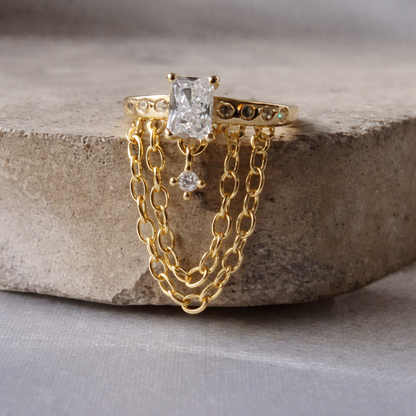 Gold chain ring with a central diamond and smaller diamonds on a stone surface
