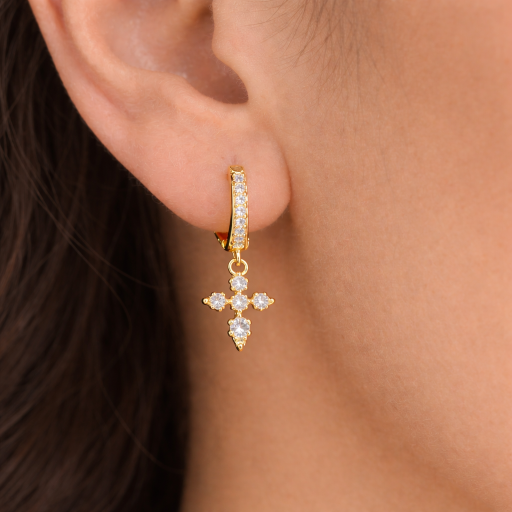Gold hoop earring with a cross design worn by a person.