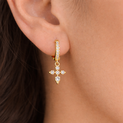 Gold hoop earring with a cross design worn by a person.