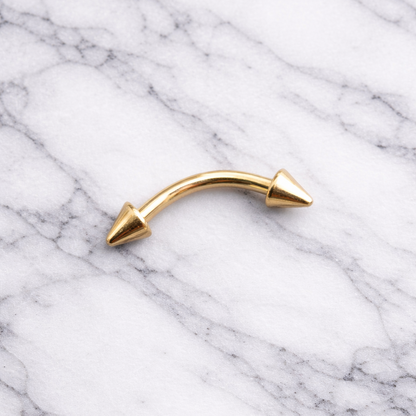 Gold curved eyebrow/rook earring with spike details on a marble background