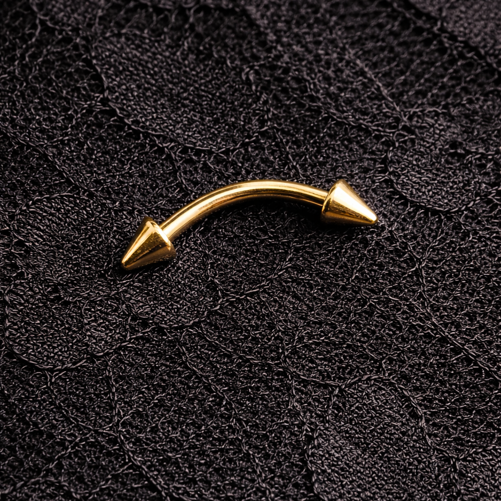 Gold curved eyebrow/rook earring with spike details on a textured black background