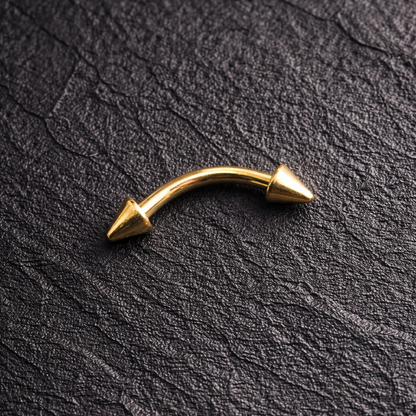 Gold curved eyebrow/rook earring with spike on a black textured background