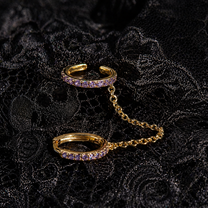 Gold ear cuff with purple gemstones on a black textured background