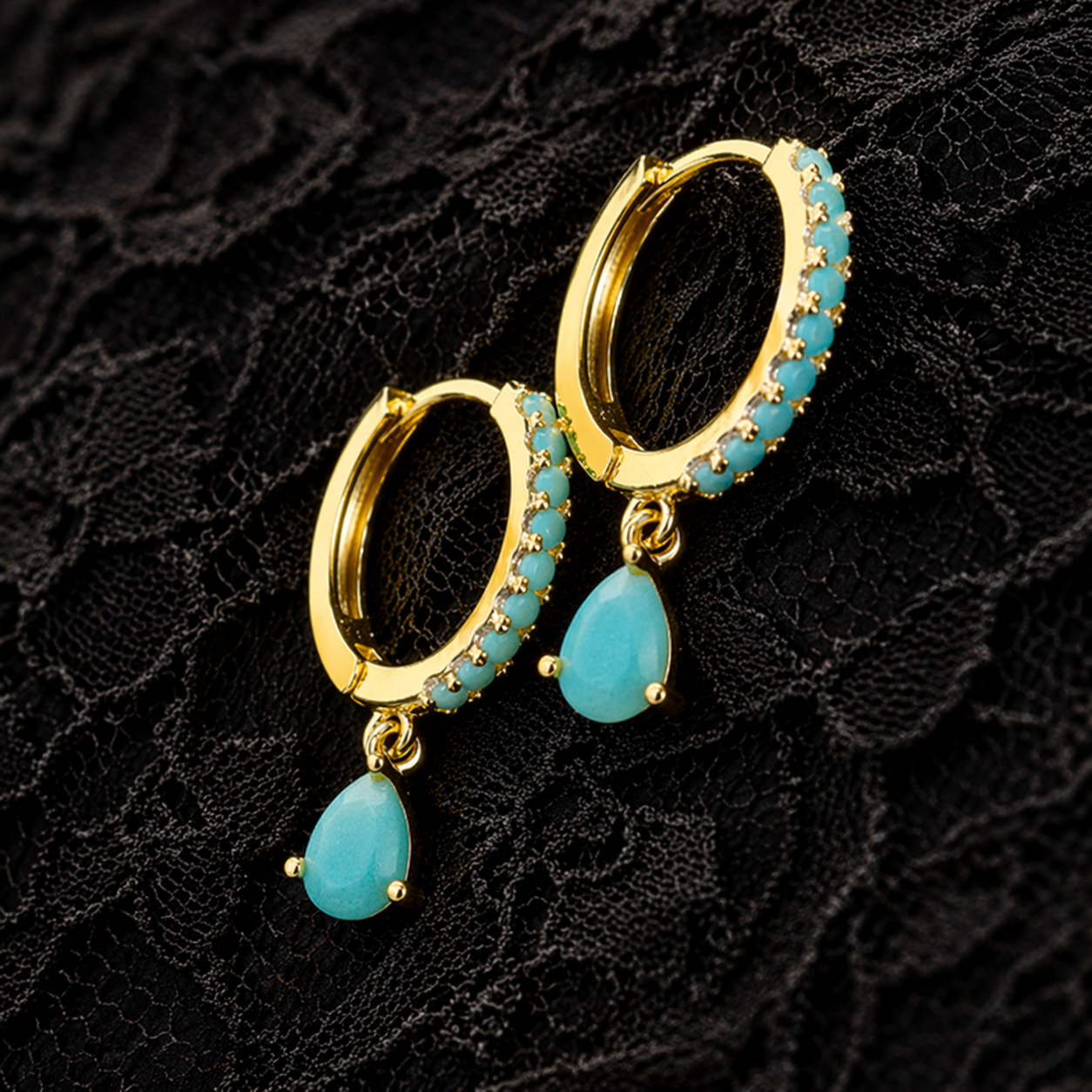 Gold hoop earrings with turquoise teardrop charms on a black lace background