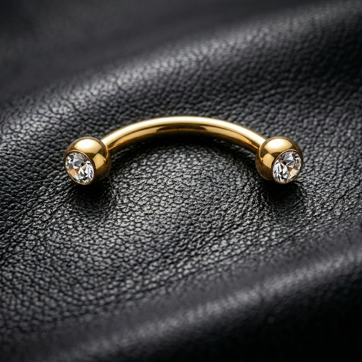 Gold eyebrow barbell with two gemstones on a black leather background