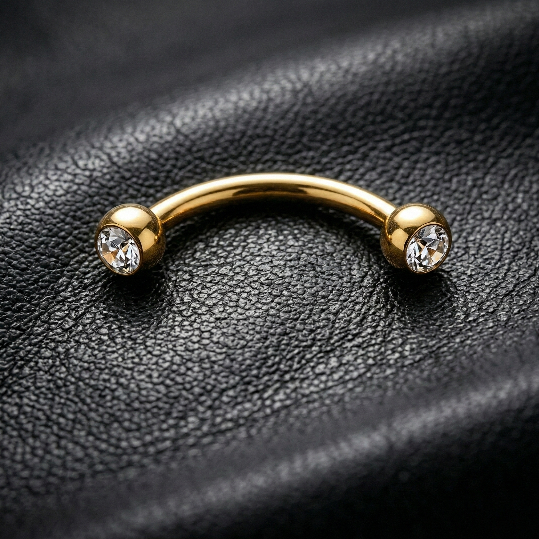 Gold eyebrow barbell with two gemstones on a black leather background