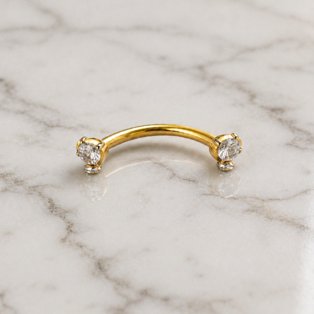 Gold eyebrow ring with three gemstones on a marble background