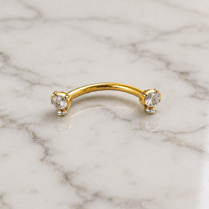 Gold eyebrow ring with three gemstones on a marble background