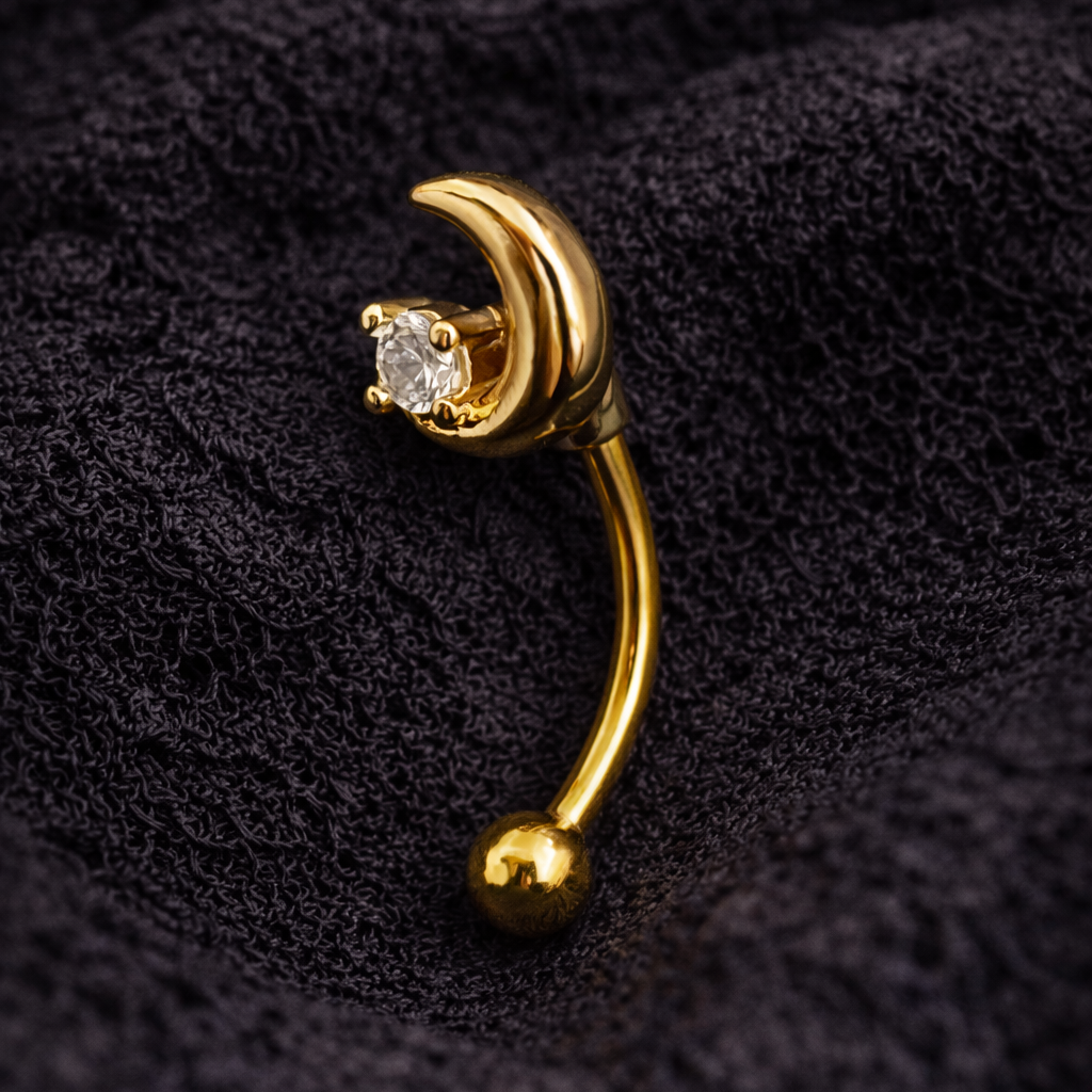 Gold eyebrow/rook bar jewellerywith a moon on a textured black background