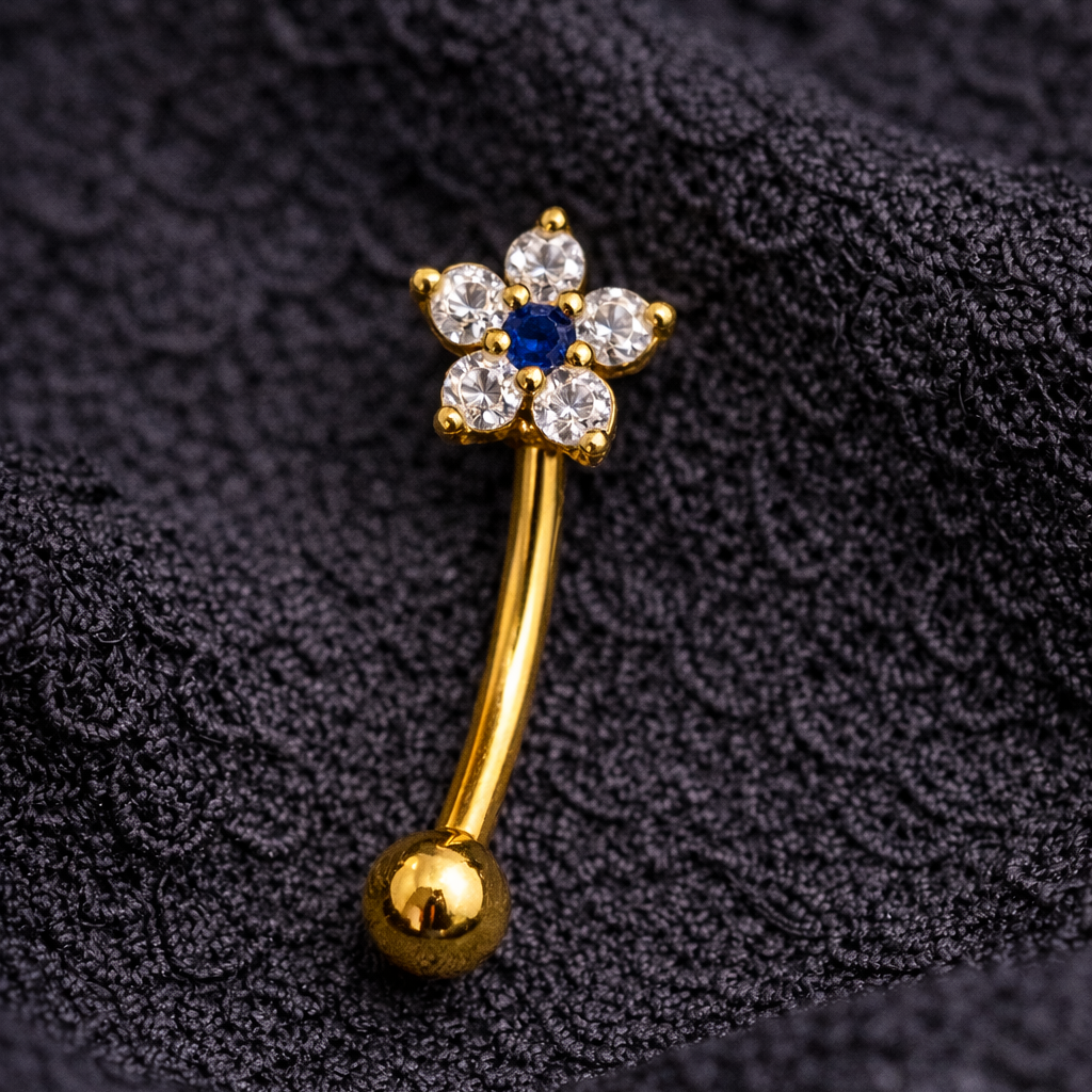 Gold eyebrow/rook bar with a blue gemstone on a textured black background