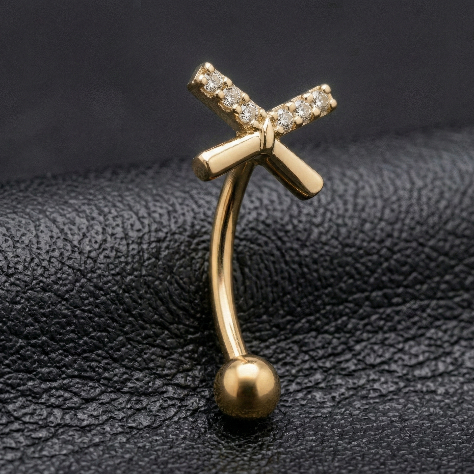 Gold eyebrow/rook bar with bow design on a black leather background