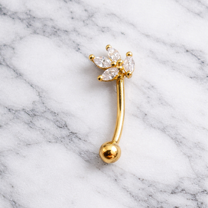 Gold eyebrow/rook bar with clear gemstones on a marble background