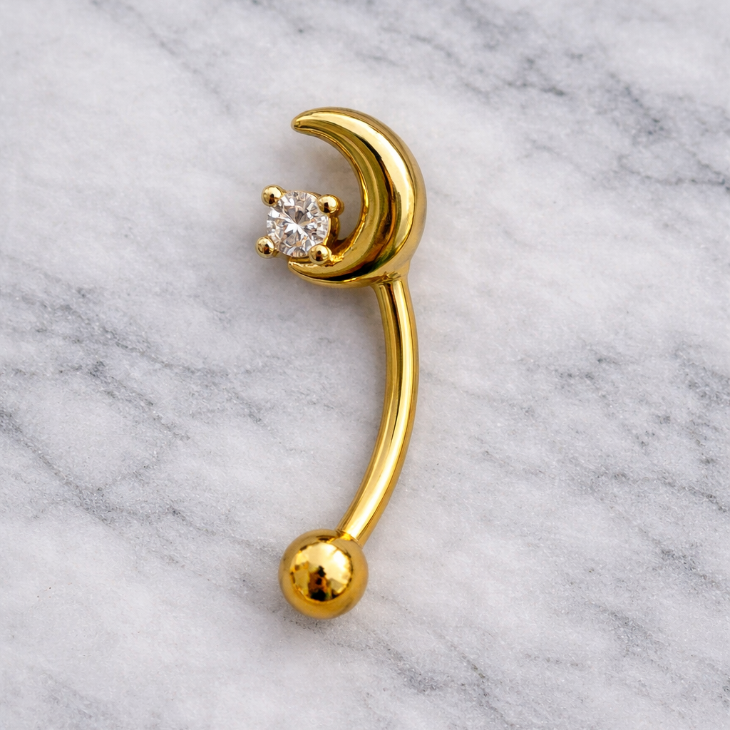 Gold eyebrow/rook bar with moon and ball design on a marble background