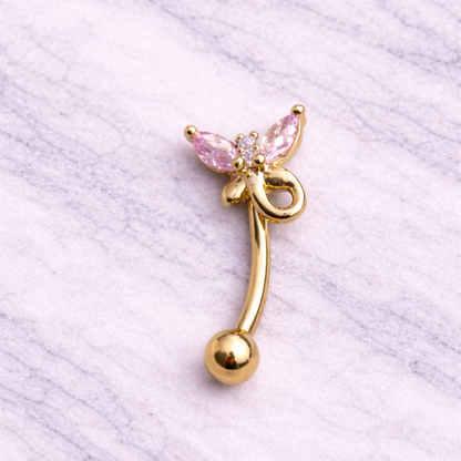 Gold eyebrow/rook bar with pink gem on a textured white background