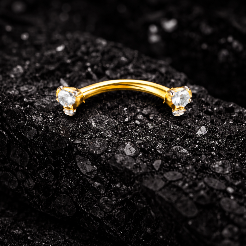 Gold eyebrow/rook bar with two gemstones on a black textured background