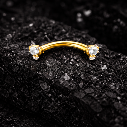 Gold eyebrow/rook bar with two gemstones on a black textured background