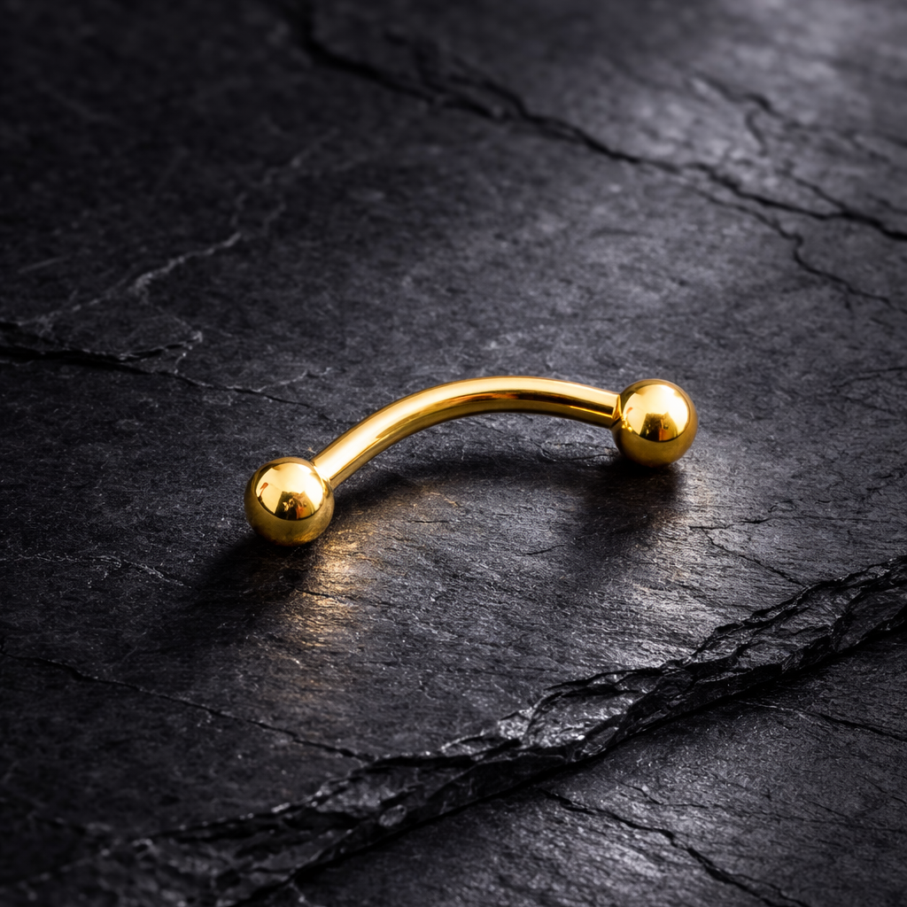 Gold eyebrow/rook barbell on a dark stone surface