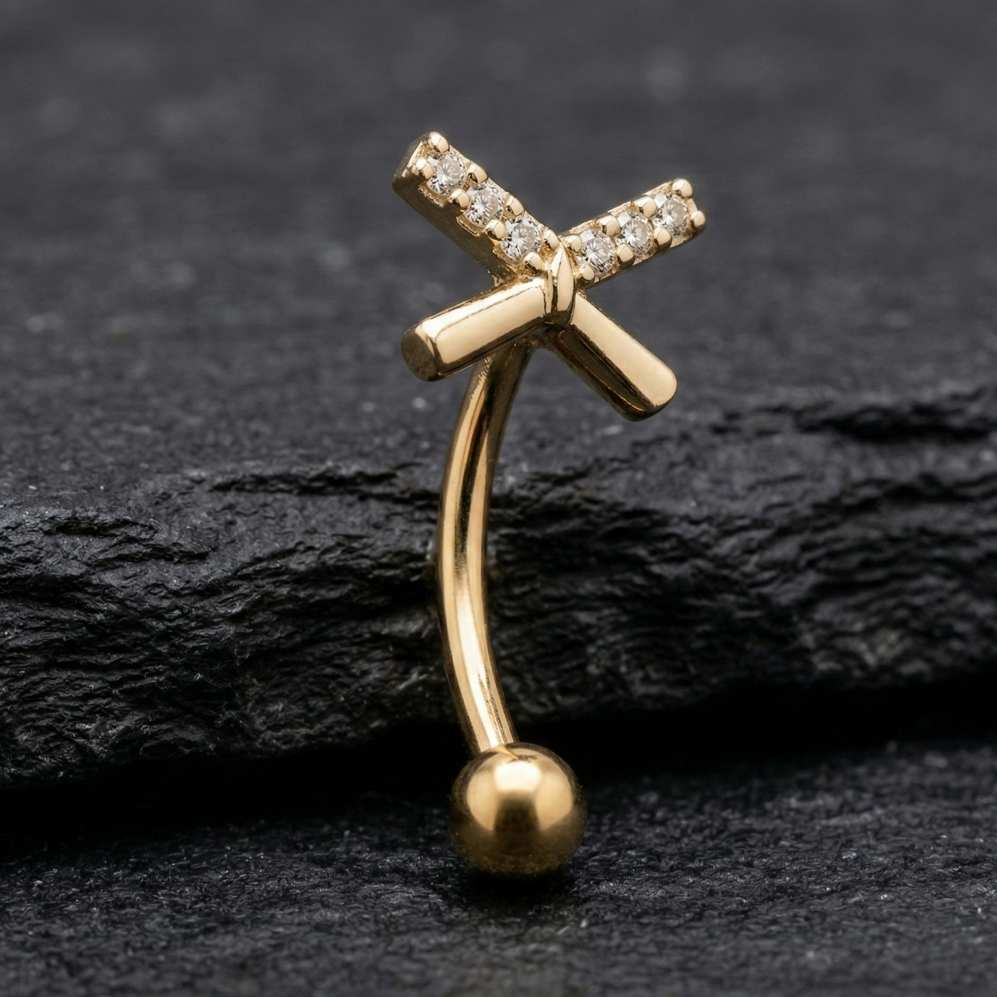 Gold eyebrow/rook barbell with bow design on a black stone background