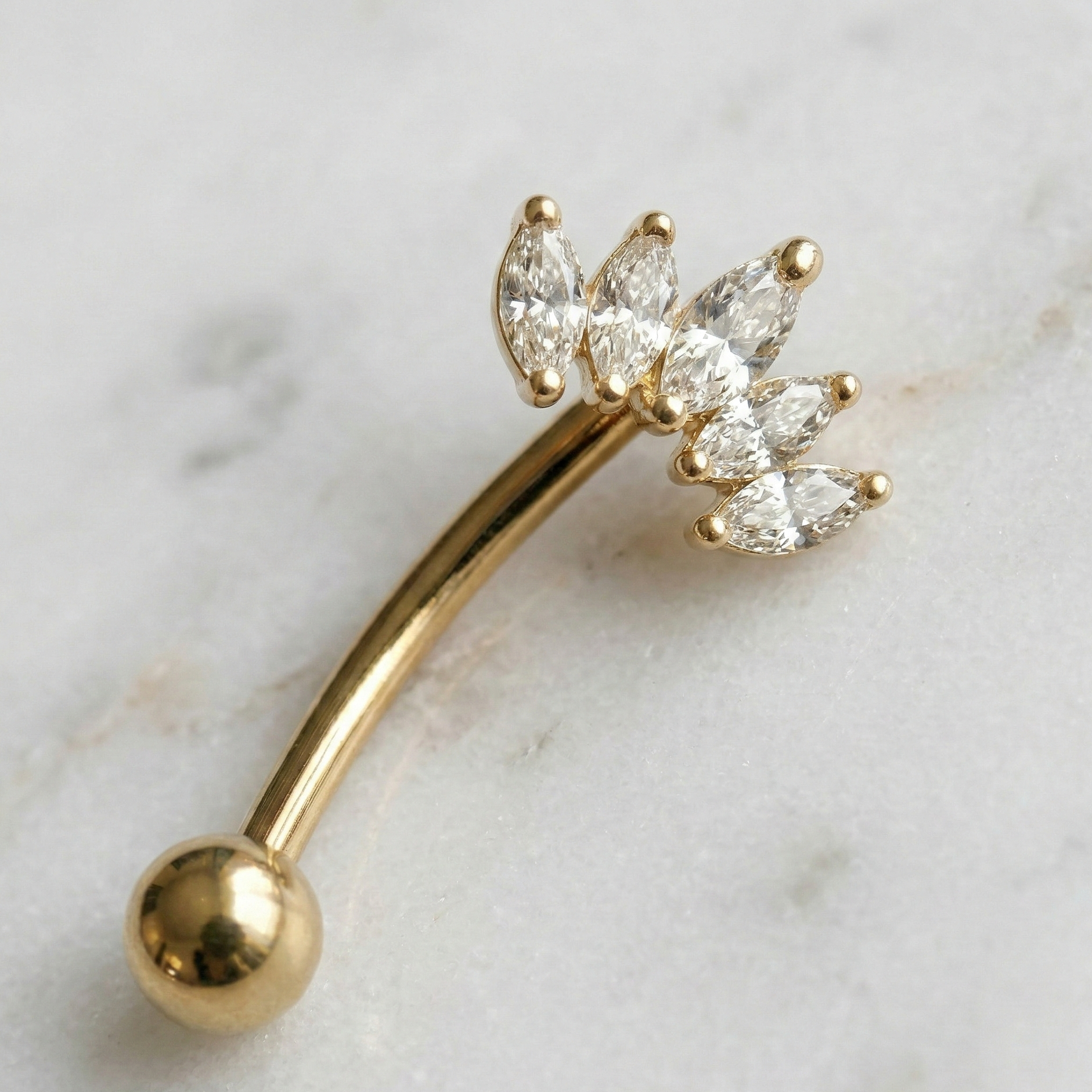 Gold eyebrow/rook barbell with crown diamond-like stones on a marble background