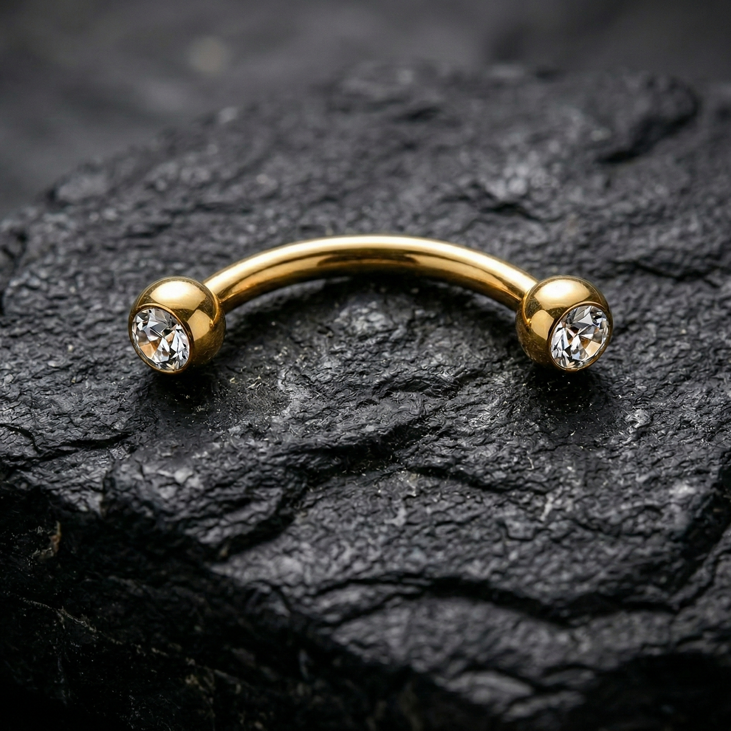 Gold eyebrow/rook barbell with crystals on a dark stone surface