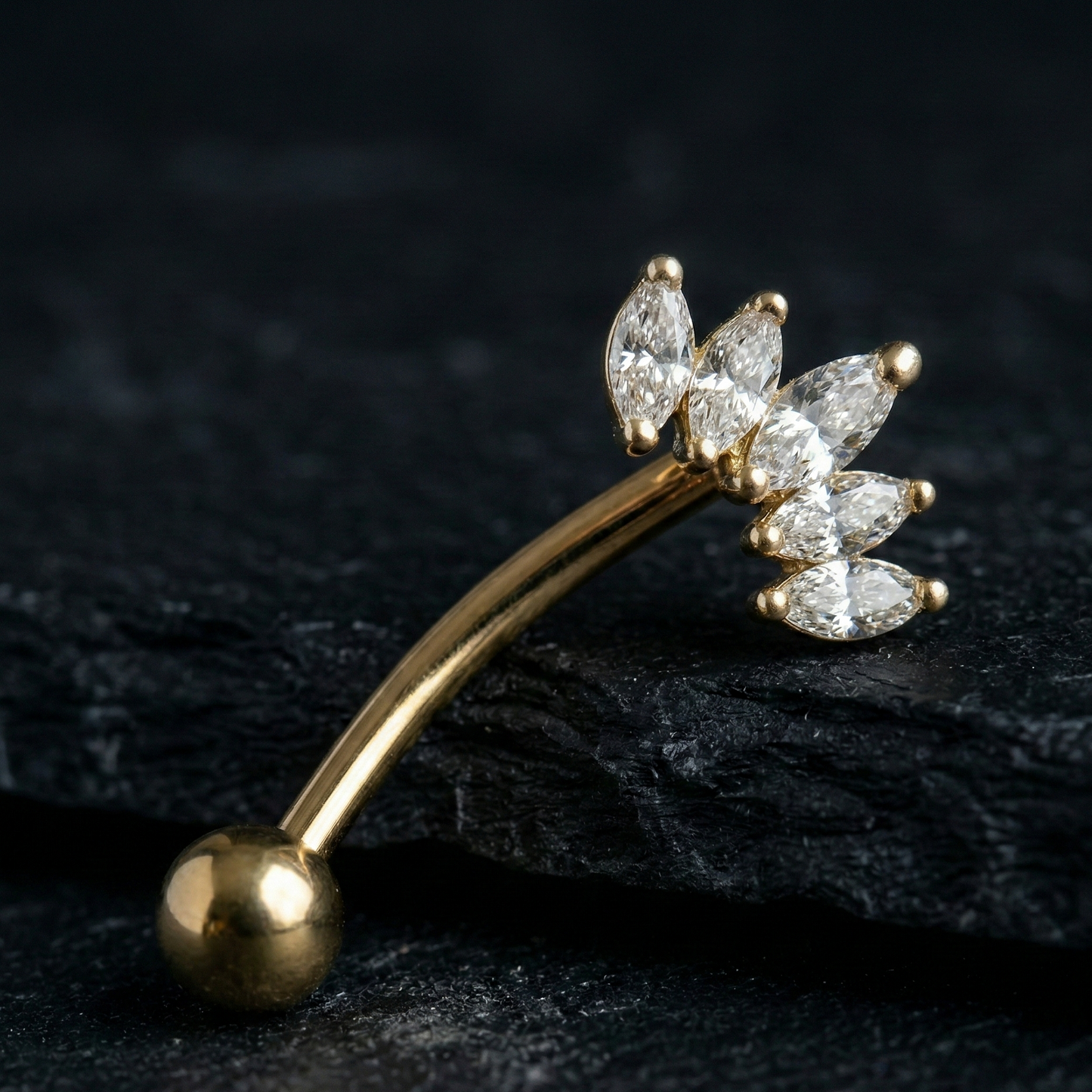 Gold eyebrow/rook barbell with diamond-like crown stones on a dark background