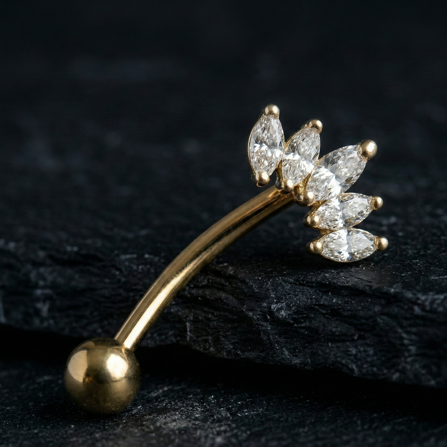 Gold eyebrow/rook barbell with diamond-like crown stones on a dark background