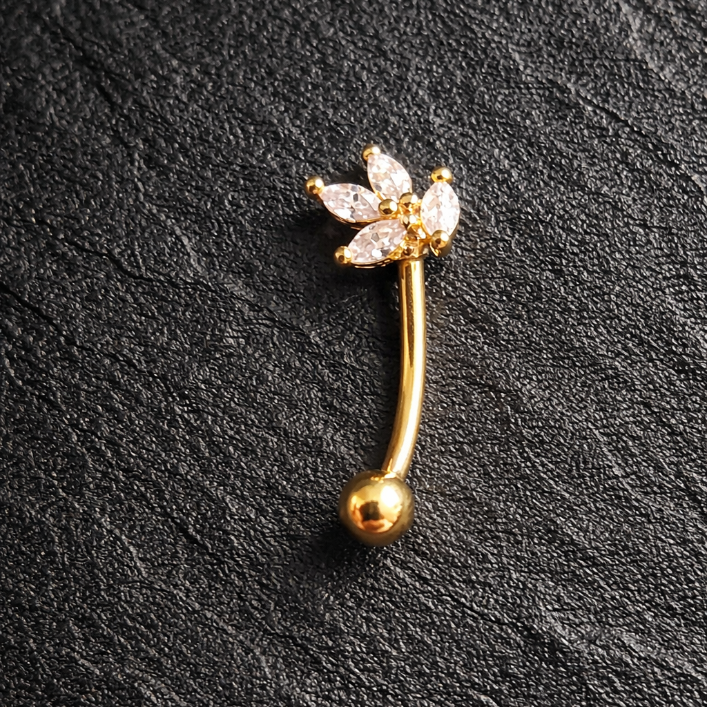Gold eyebrow/rook barbell with floral design on a black textured background
