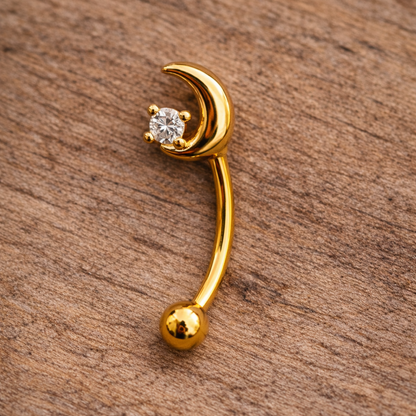 Gold eyebrow/rook barbell with moon design on a wooden surface