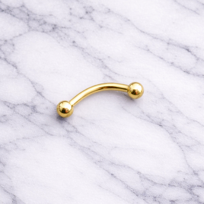 Gold eyebrow/rook piercing bar on a marble background