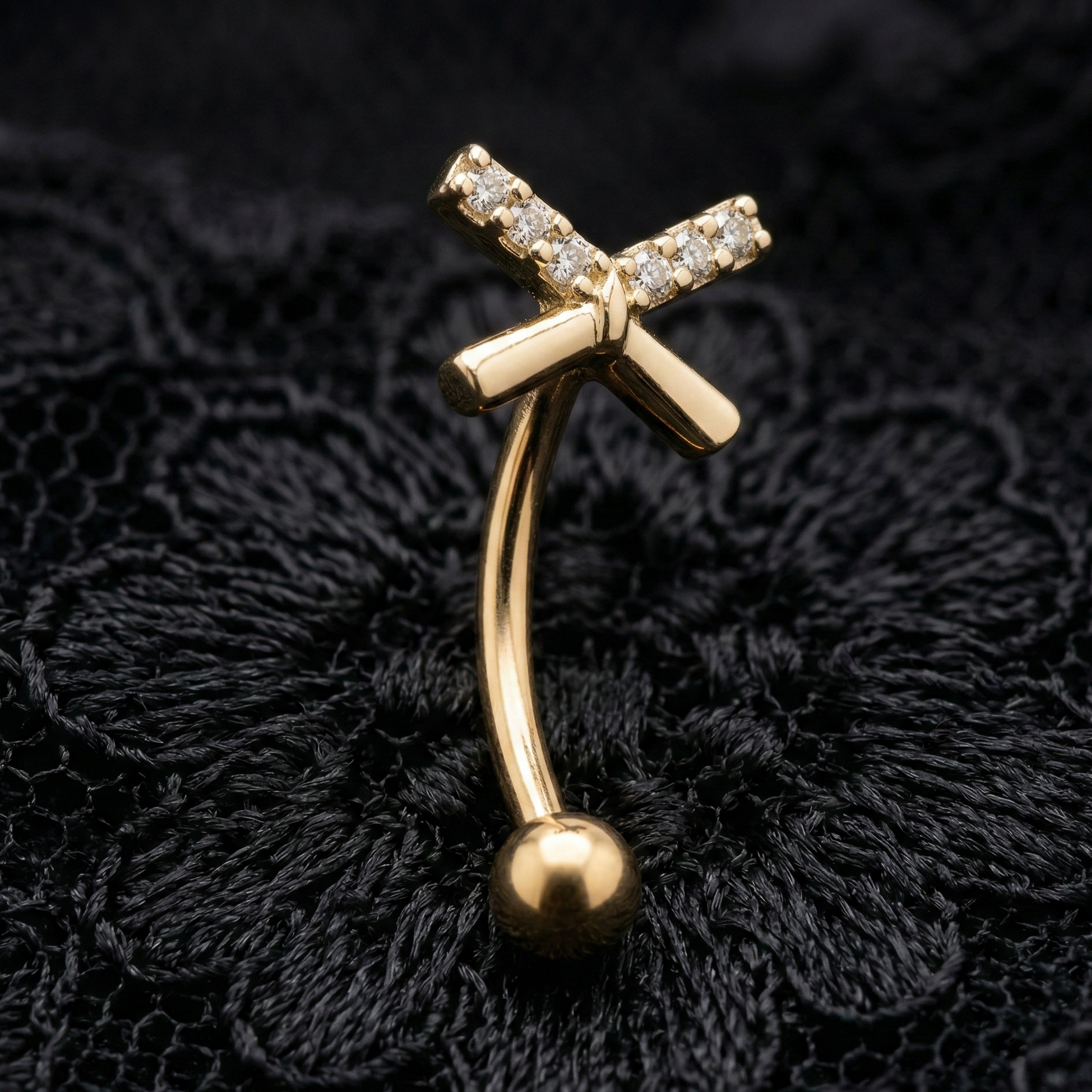 Gold eyebrow/rook piercing bar with a bow design on a black lace background