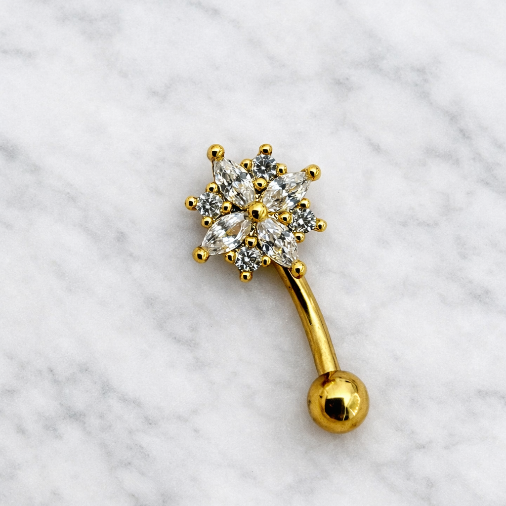 Gold eyebrow/rook piercing bar with clear gemstones on a marble background
