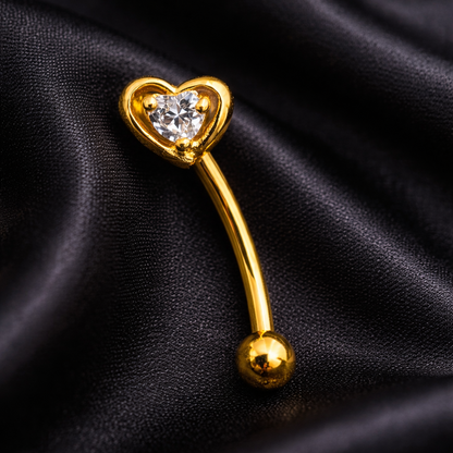 Gold eyebrow/rook piercing bar with heart-shaped gem on black satin background