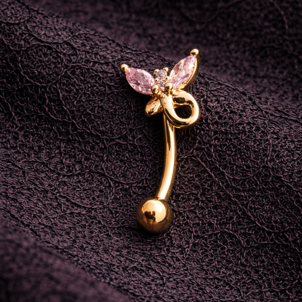 Gold eyebrow/rook piercing bar with pink gemstone on a dark textured background