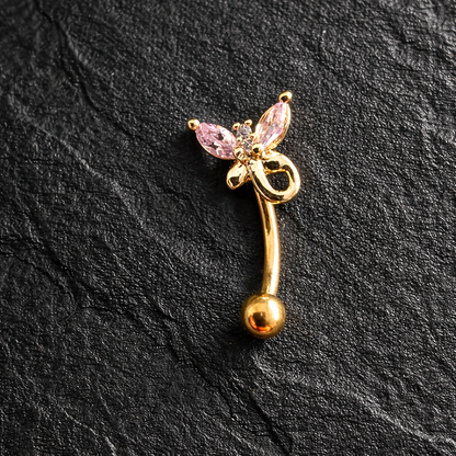 Gold eyebrow/rook piercing barbell with pink gemstones on a black stone surface