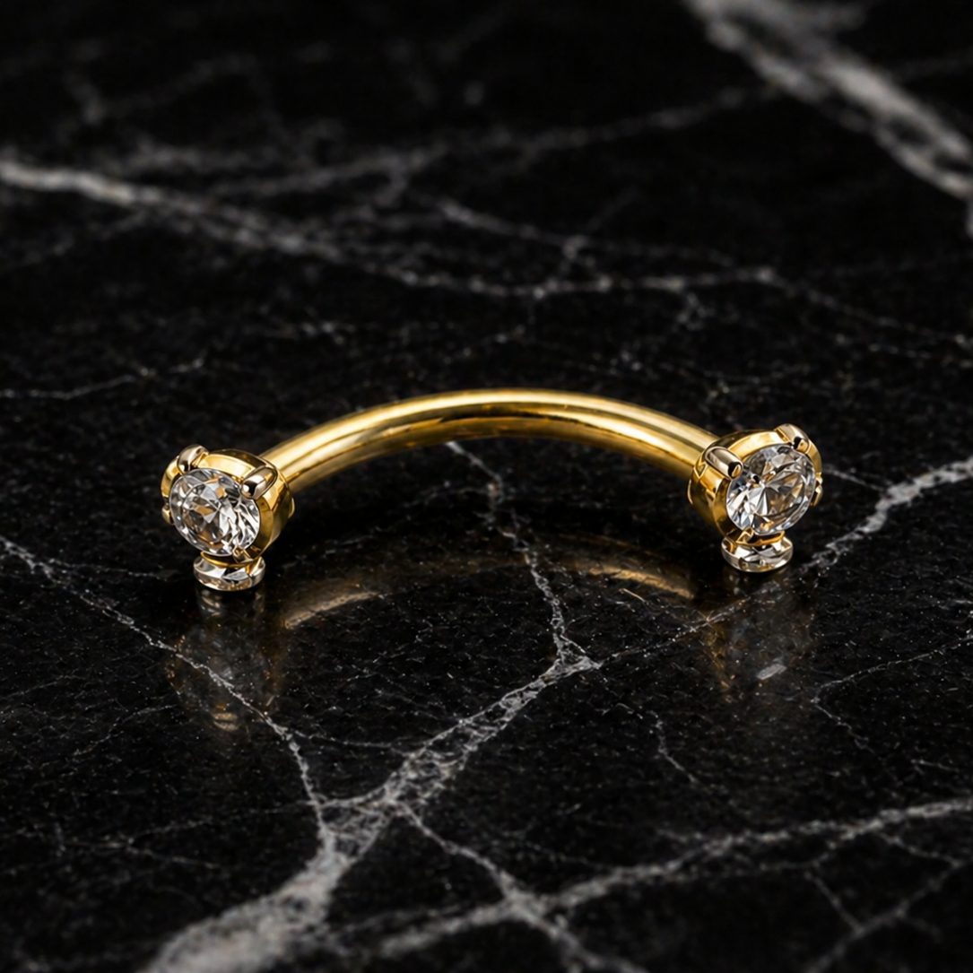 Gold eyebrow/rook ring with three diamonds on a black marble surface
