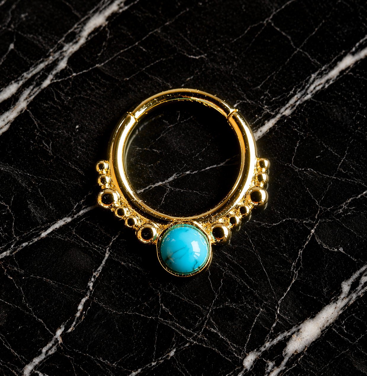 Gold hoop earring with a turquoise stone on a black marble background