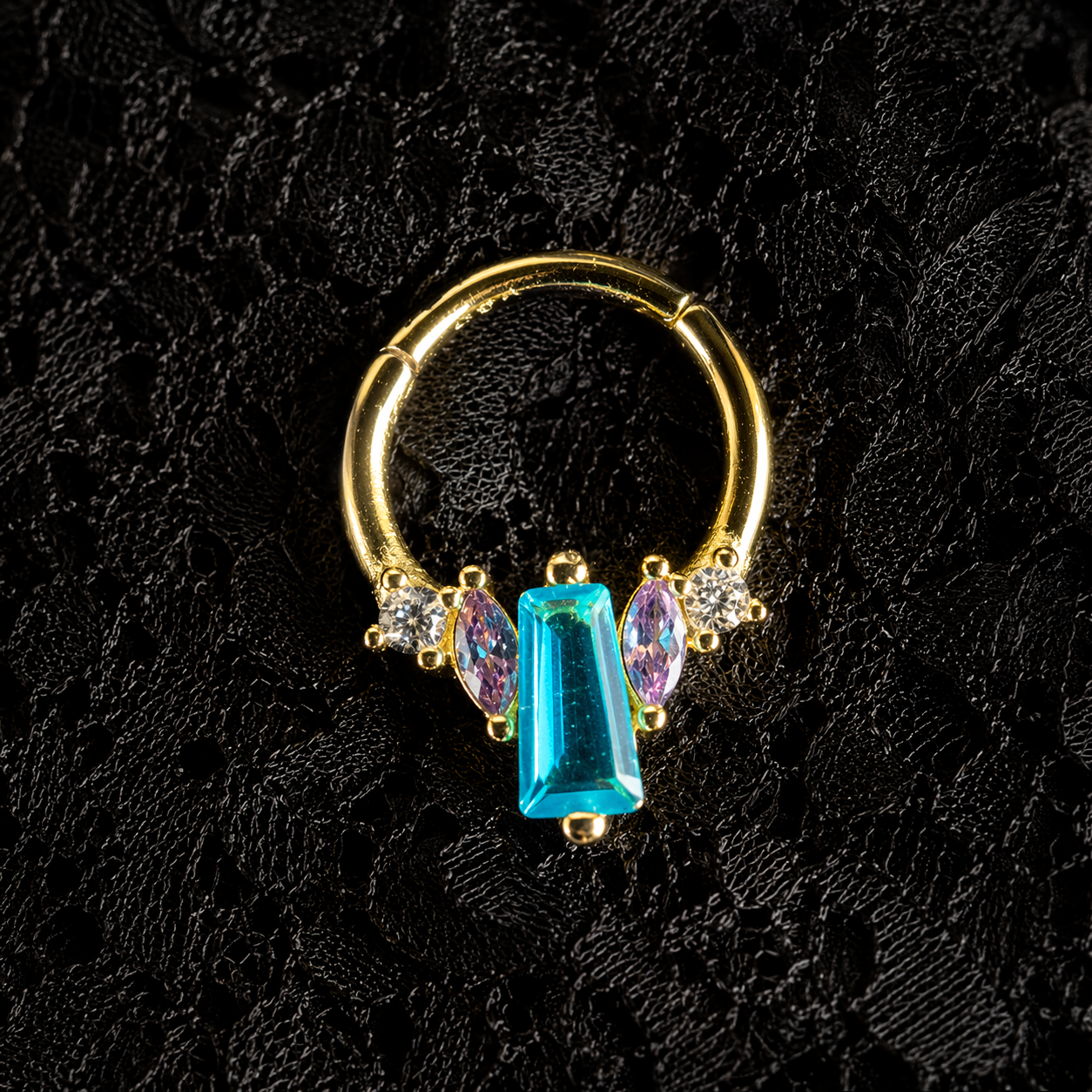 Gold hoop earring with blue and purple gemstones on a black textured background