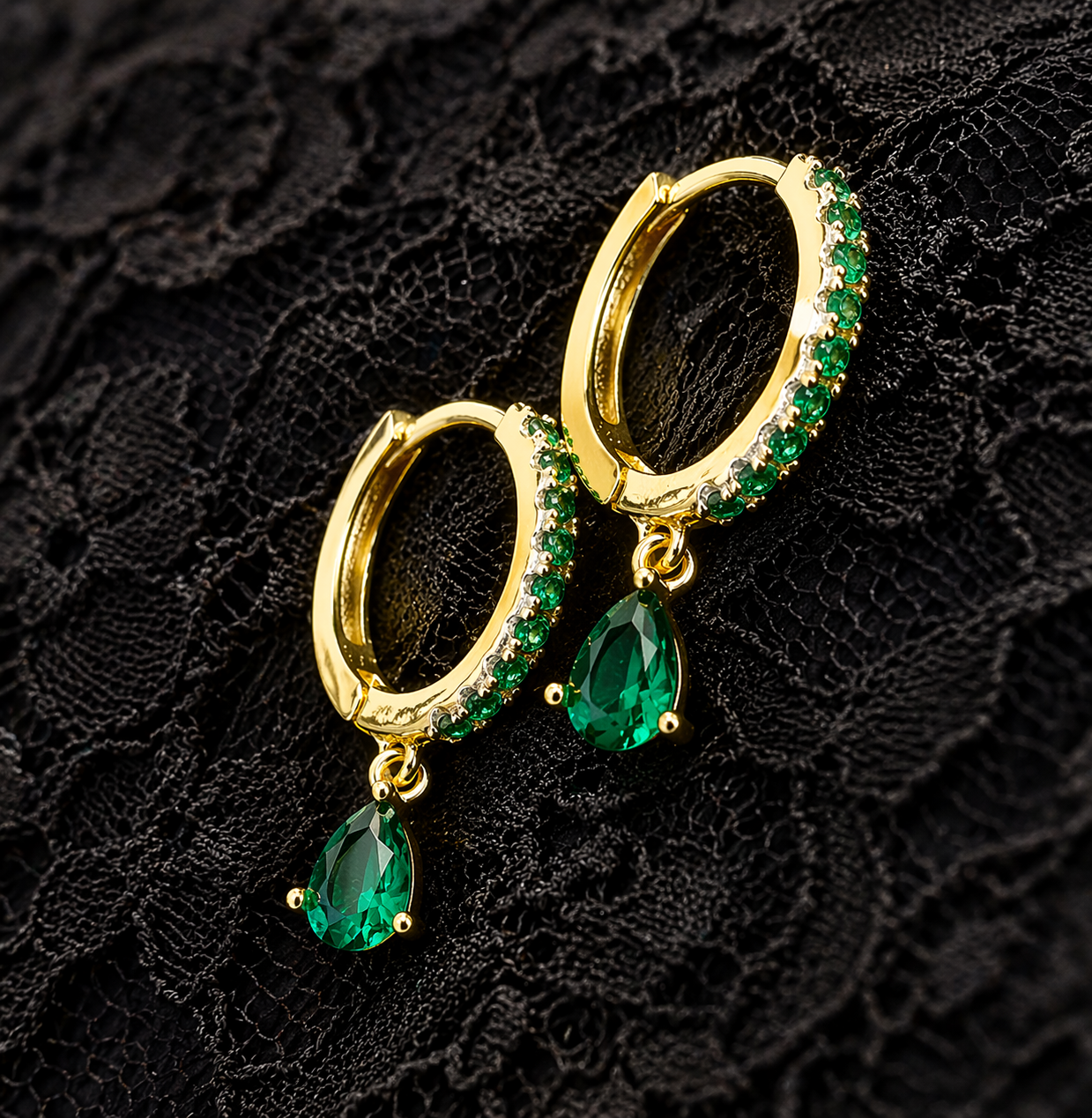 Gold hoop earrings with green gemstones on a black lace background