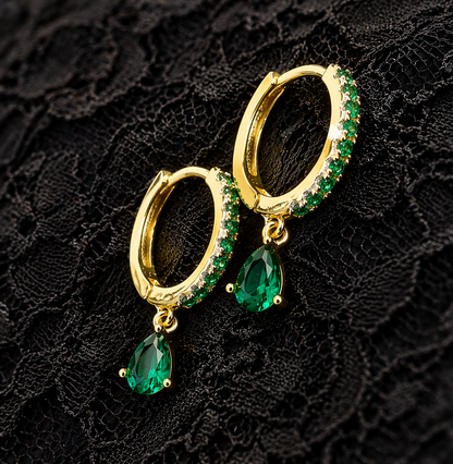 Gold hoop earrings with green gemstones on a black lace background