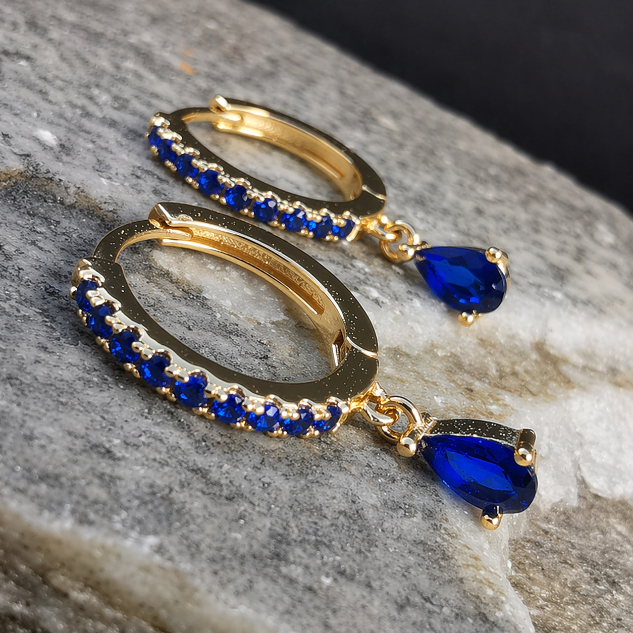 Gold hoop earrings with blue gemstones on a stone surface